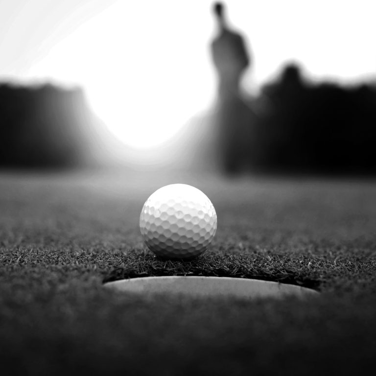Golf balls and golf club on green grass shiny light sunse