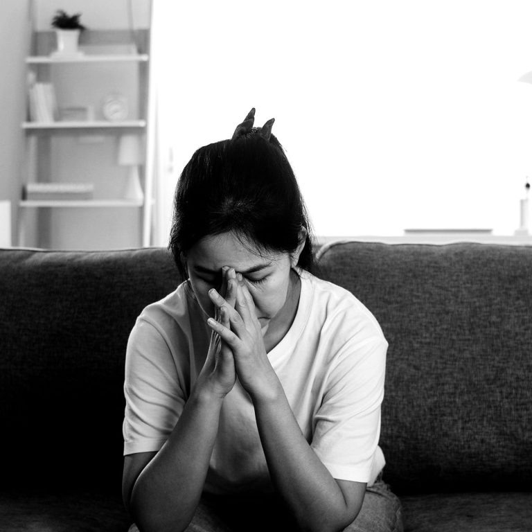 Depressed crying Asian business woman stressed with headache sitting on sofa in living room at house when social distancing stay at home and self quarantine time, coronavirus concept.