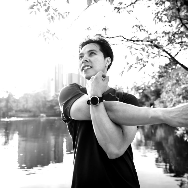 Healthy Asian man stretching his shoulder after finished running outdoor in the park in morning