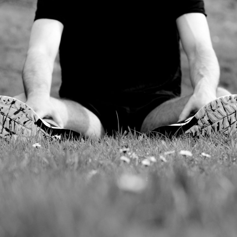 A super close up of training shoes while stretching legs over the grass of the park during a training day