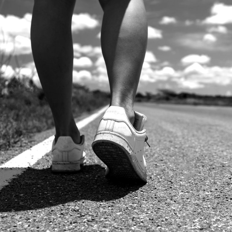 Woman is walking on small country road street with blue sky background.